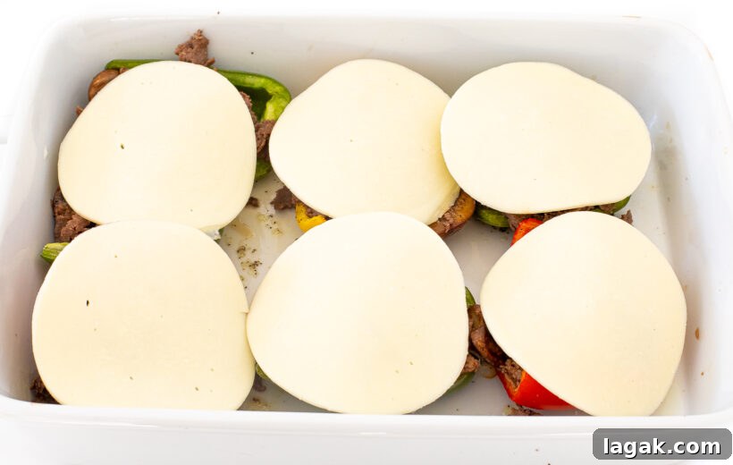 Philly Cheesesteak Stuffed Bell Peppers: Savory Low-Carb Dinner 11 Stuffed Peppers with cheese slices on top in a white baking pan.