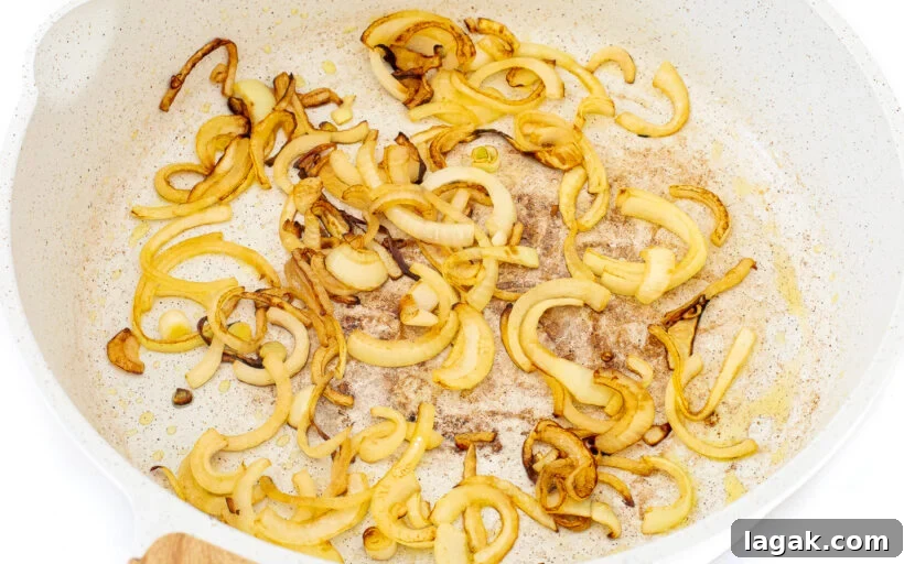 Philly Cheesesteak Stuffed Bell Peppers: Savory Low-Carb Dinner 6 Sauteed sliced onions in a white frying pan.