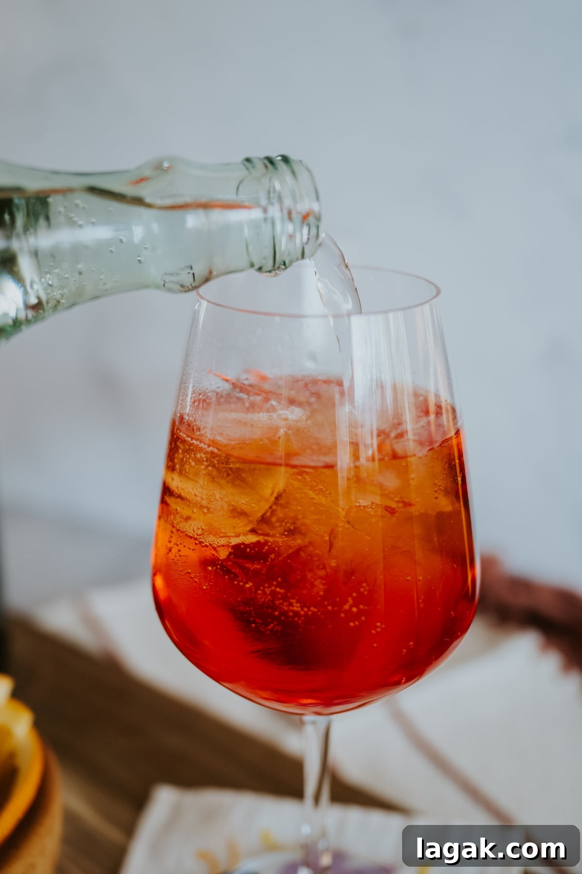 Classic Aperol Spritz Recipe: How to Make the Perfect Cocktail 6 process shot of pouring topo chico into the glass with the ice, cava, and aperol.