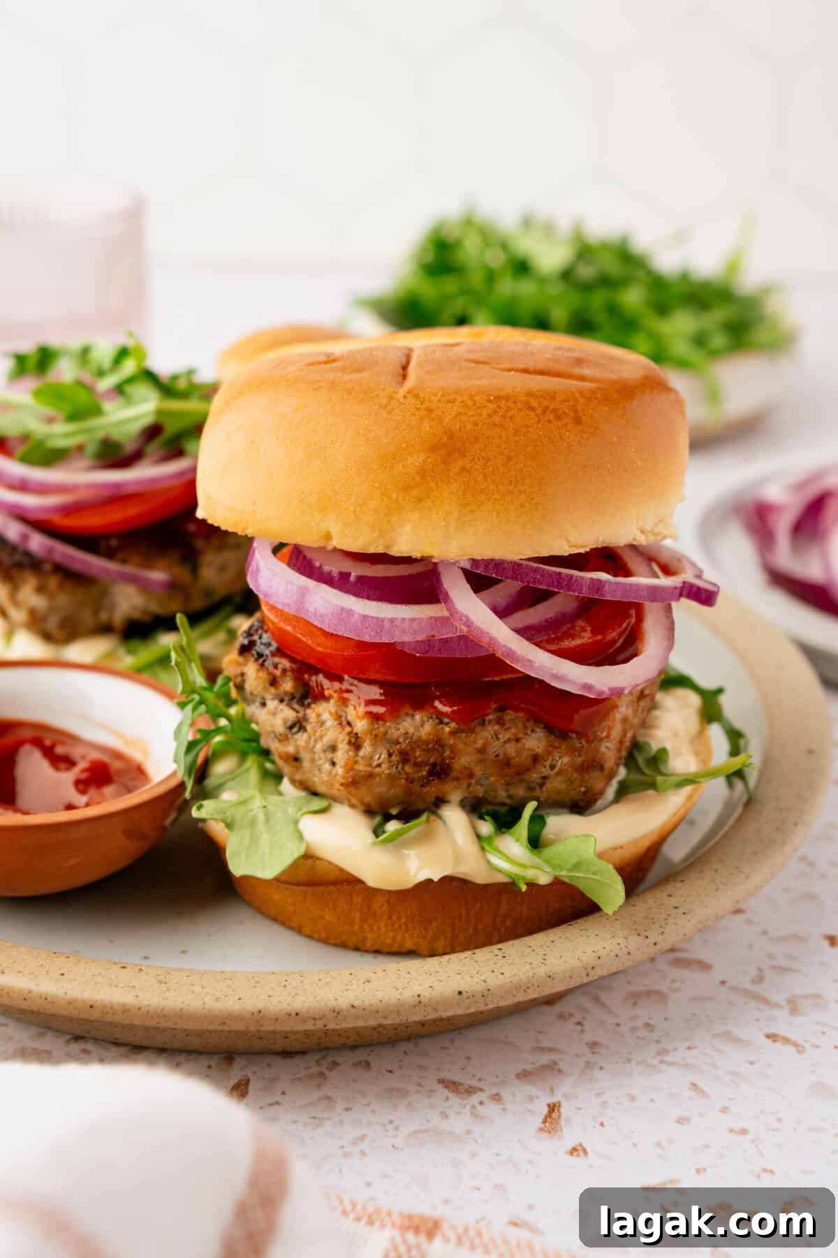 Juicy Ground Pork Burger Recipe for Flavorful Weeknight Meals 2 A burger in a bun topped with ketchup, mayonnaise, chopped tomatoes, onions and lettuce.