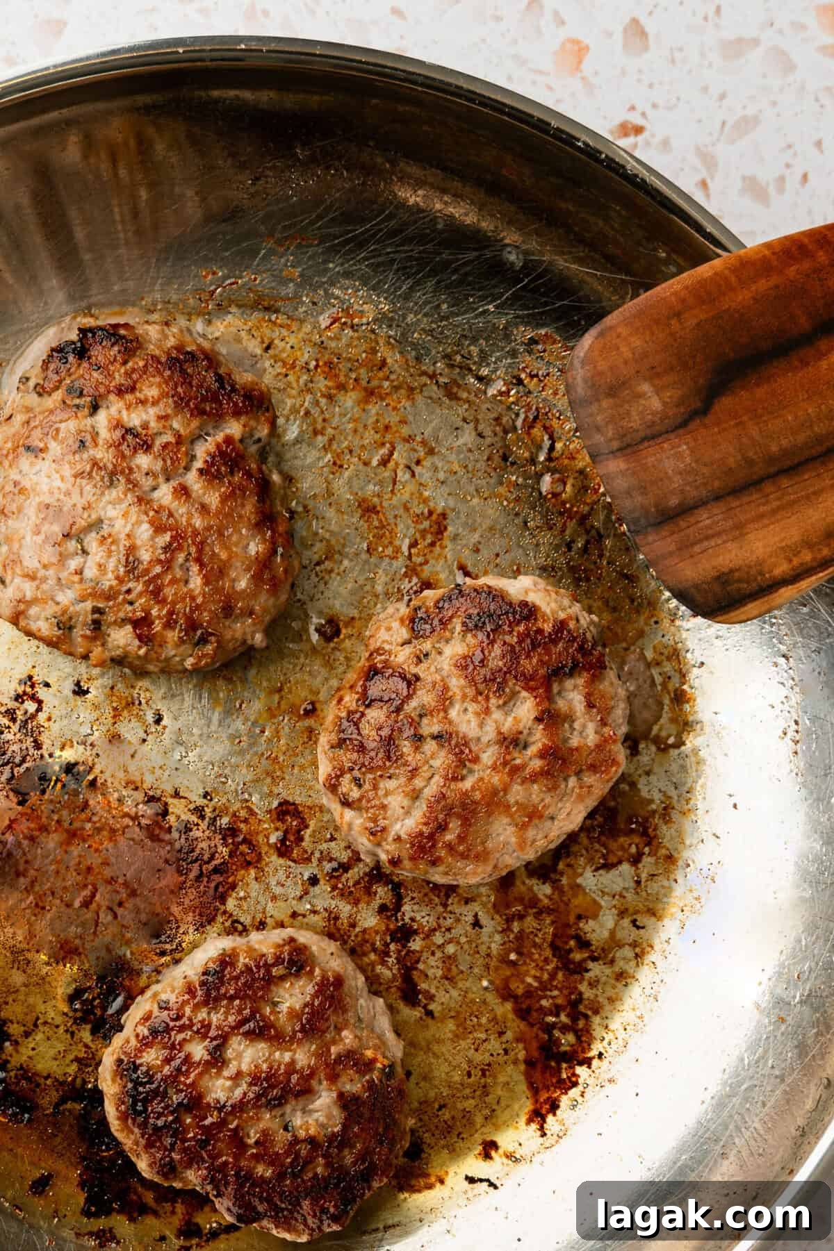 Juicy Ground Pork Burger Recipe for Flavorful Weeknight Meals 7 Cooked burger patties in a skillet with a wooden spatula in the pan next to the burgers.