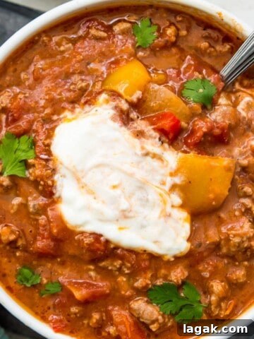 A bowl of chili topped with sour cream with a spoon in it.