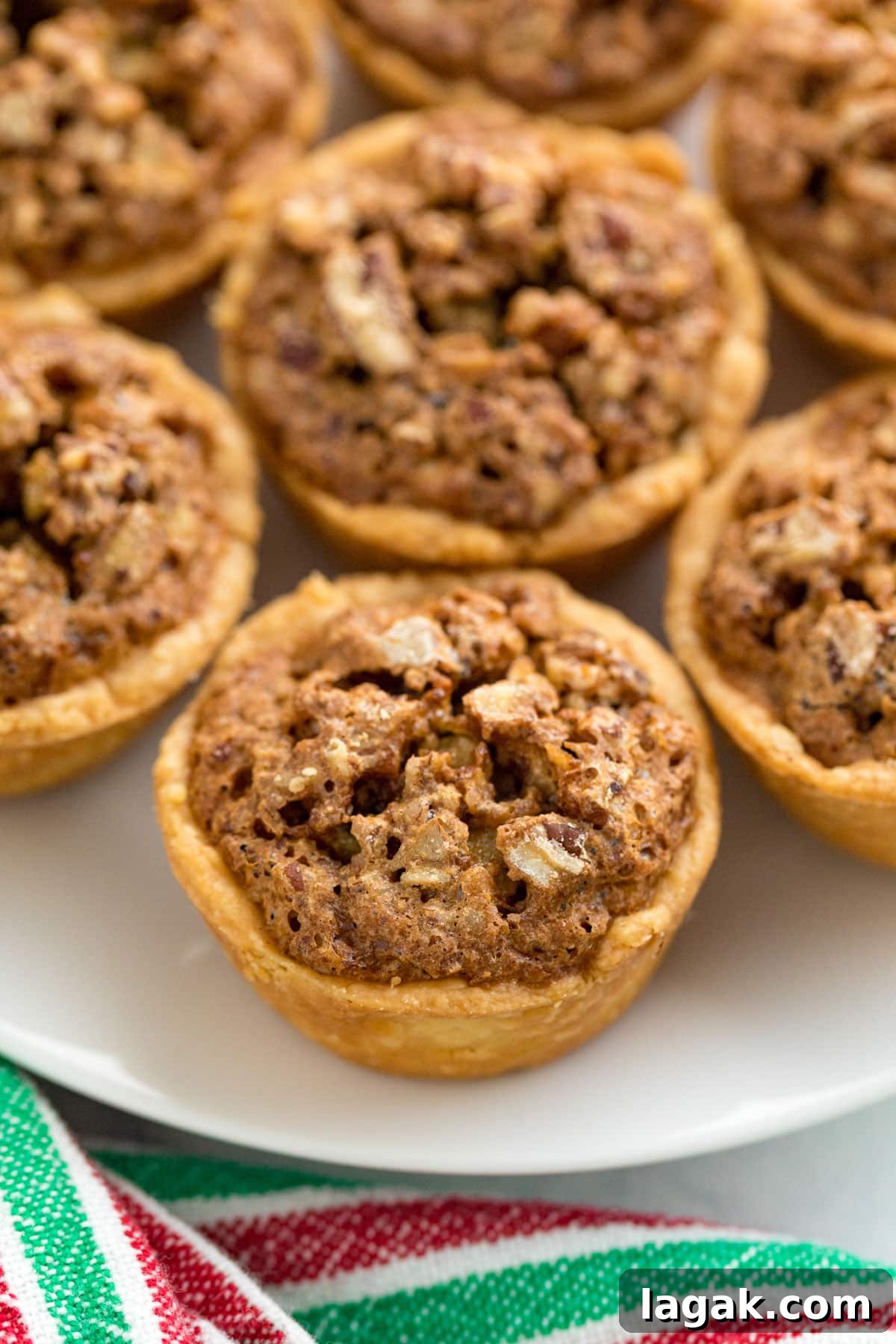 Grandma Rose’s Pecan Tassies Recipe for Perfect Bite-Sized Pies 14 A close up image of pecan tassies on the side of a white plate.