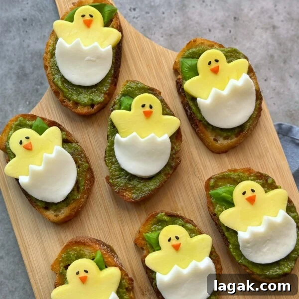 Easter Burrata Caprese Salad with Fresh Herbs and Tomatoes 4 Seven pieces of toast with green pesto are topped with cheese slices shaped like cartoon chicks hatching from eggs, creating fun bites perfect for kids’ food recipes and healthy party dishes, arranged on a wooden serving board.
