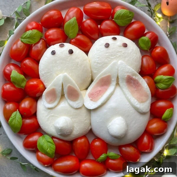 Easter Burrata Caprese Salad with Fresh Herbs and Tomatoes 5 A plate with two bunny-shaped mozzarella bites decorated with cheese and pink ears, black eyes, and surrounded by cherry tomatoes and fresh basil leaves—perfect for fun, health-conscious food recipes.