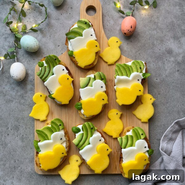Easter Burrata Caprese Salad with Fresh Herbs and Tomatoes 6 A wooden board holds slices of bread topped with avocado, egg, and chick-shaped decorations—perfect for fun food recipes or healthy bites. Yellow chick marshmallow candies and colored Easter eggs add a festive touch.