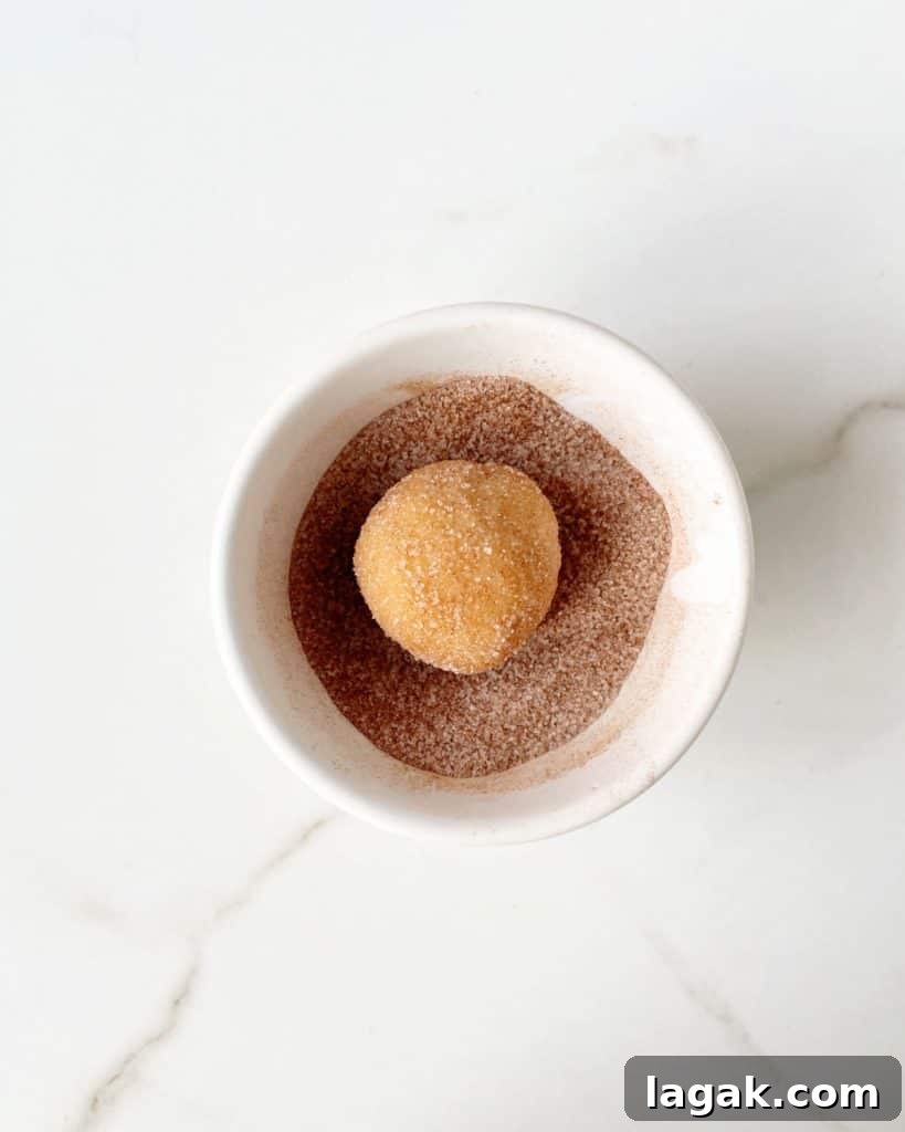 Chewy Browned Butter Snickerdoodle Cookies Recipe 8 Snickerdoodle cookie ball coated in cinnamon sugar in a white bowl on a white marble surface.
