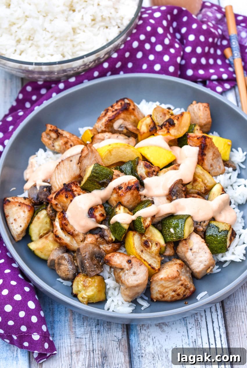 air fryer hibachi chicken and vegetables over steamed rice and topped with yum yum sauce on a gray plate
