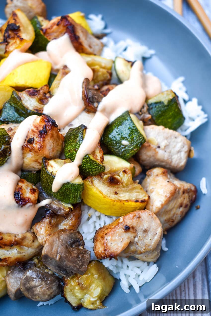 air fryer hibachi chicken and vegetables over steamed rice and topped with yum yum sauce on a gray plate