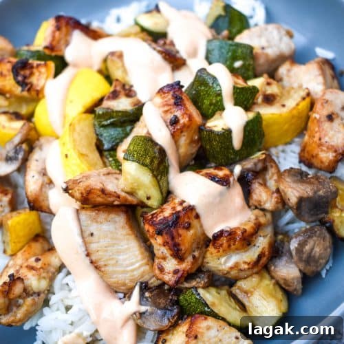 air fryer hibachi chicken and vegetables over steamed rice and topped with yum yum sauce on a gray plate