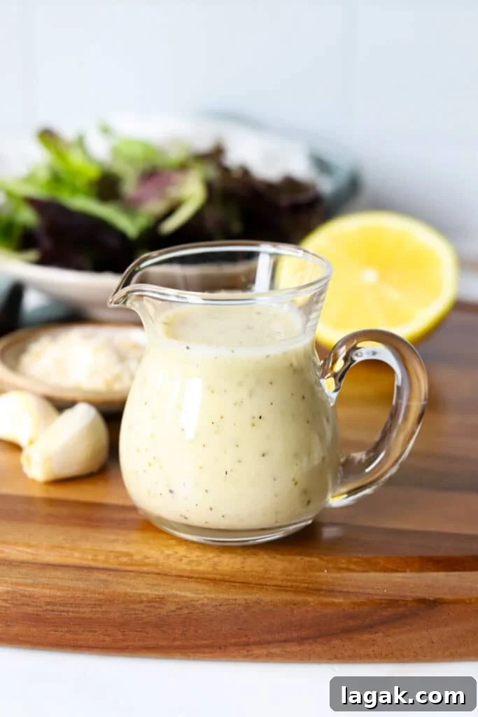Garlic Parmesan Dressing Recipe for Salads and Veggies 2 Garlic parmesan dressing in a glass container with garlic and lemon on a wooden board.