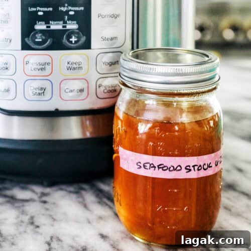 mason jar of seafood stock in front of an Instant Pot on marble.