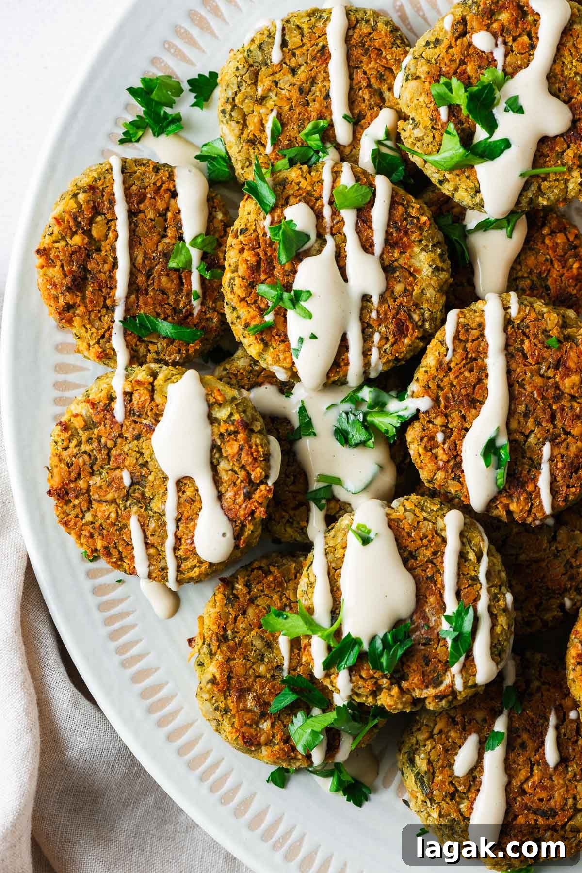 Crispy Baked Falafel Using Canned Chickpeas 2 Top down view of a serving bowl with baked falafel made with canned chickpeas drizzled with tahini sauce.