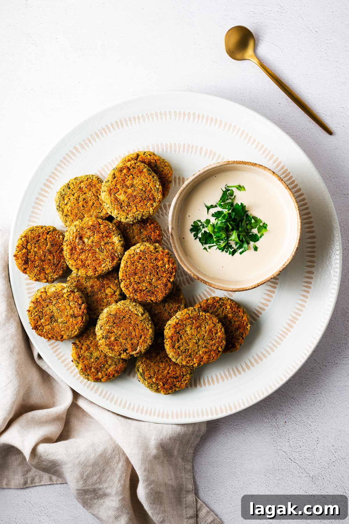 Crispy Baked Falafel Using Canned Chickpeas 11 A white serving bowl with baked falafel and tahini sauce viewed from above.