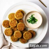 Crispy Baked Falafel Using Canned Chickpeas 12 Baked falafel patties on a white serving plate with falafel sauce in a small bowl.