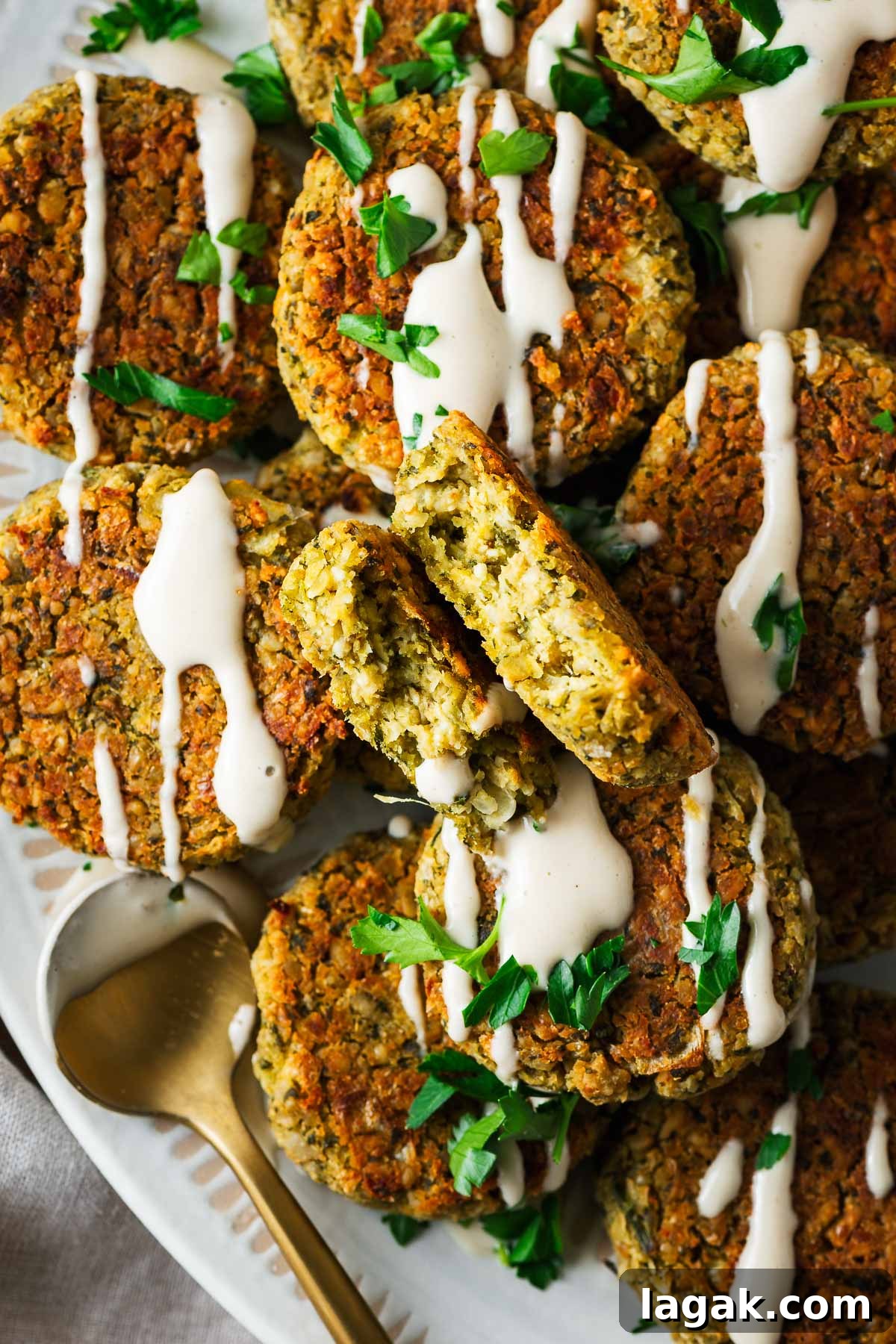 Crispy Baked Falafel Using Canned Chickpeas 3 A falafel patty broken in half to expose the texture surrounded by more whole falafel patties.