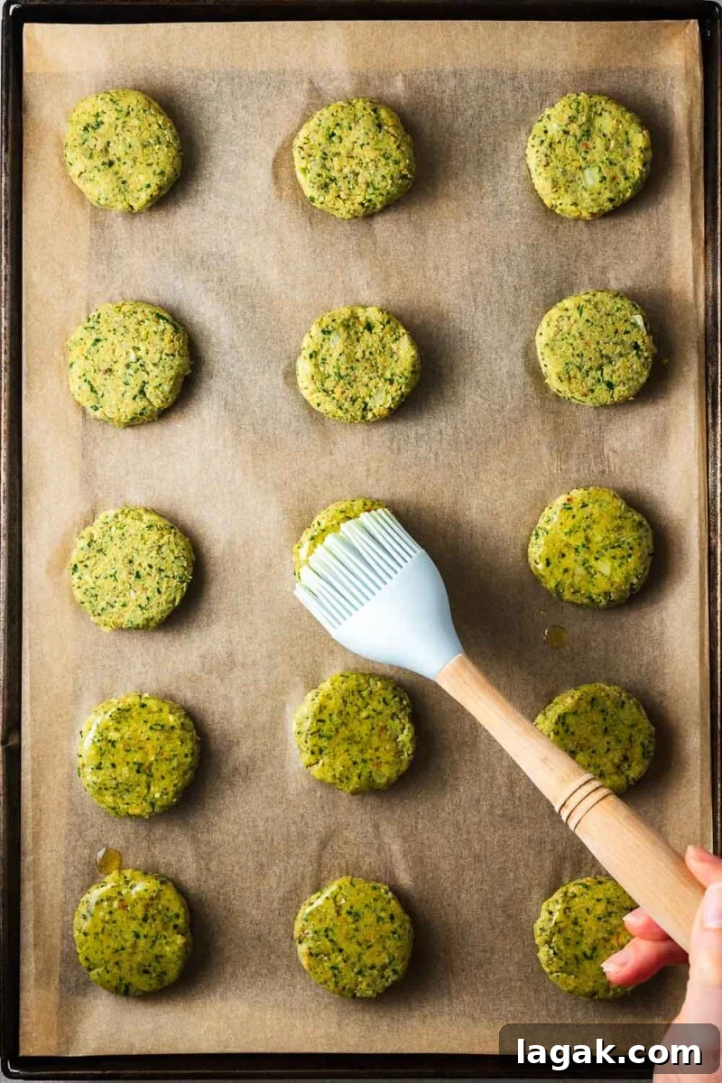 Crispy Baked Falafel Using Canned Chickpeas 9 Brushing falafel patties arranged on a parchment-lined baking sheet with olive oil.