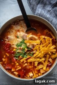 gray bowl of chicken tortilla soup topped with tortilla strips, melted cheese and cilantro