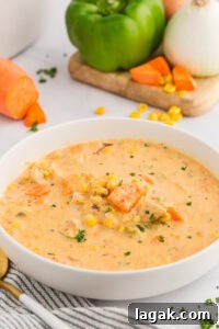 White shallow bowl of chowder with corn and sweet potatoes with green pepper, onion and sweet potato in background