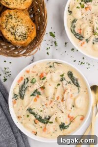 overhead view of two bowls of chicken gnocchi soup with basket of garlic bread, dishcloth and spoons on side