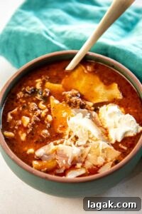 Slow Cooker Lasagna Soup garnished with cheese and served in bowl with wooden spoon