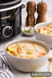 side view of bowl of chicken noodle soup surrounded by wooden salt and pepper shakers, another bowl of soup, gold spoons, and black slow cooker