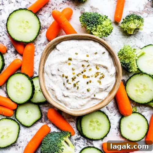 Ranch in a gray bowl with veggies surrounding it on a white counter.