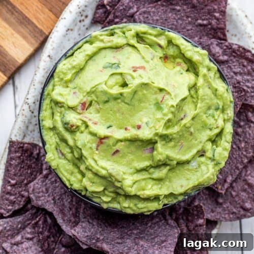 Overhead shot of guacamole in black bowl with blue chips on a white counter.
