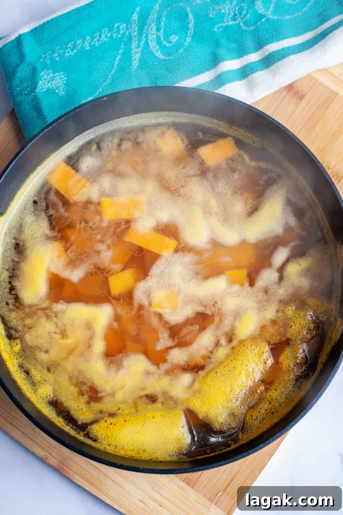 Mississippi Chicken Served Over Creamy Mashed Sweet Potatoes 11 Cubed sweet potatoes boiling in a large pot of water on the stove, with steam rising as they cook, set on a wooden cutting board with a teal kitchen towel nearby.