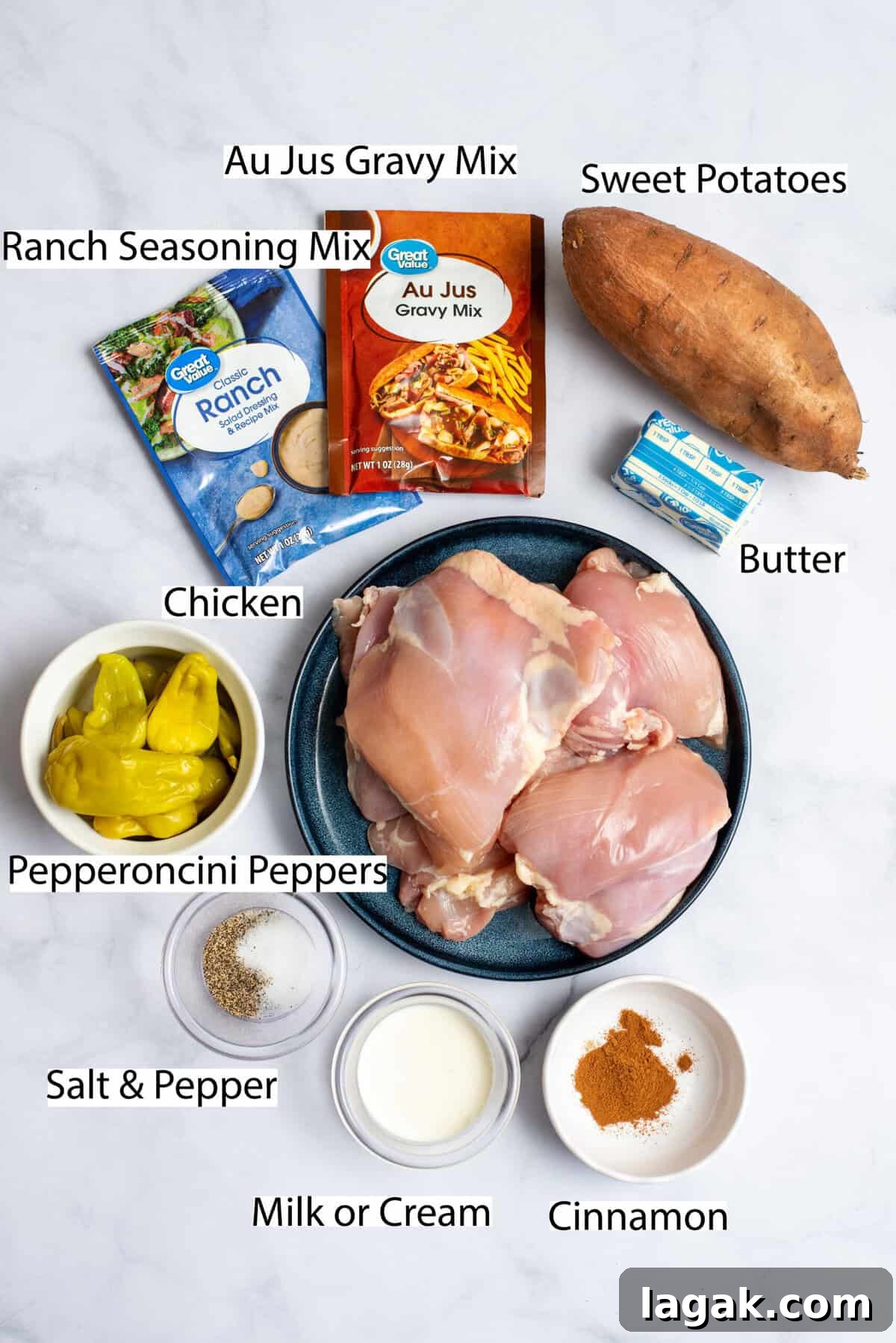 Mississippi Chicken Served Over Creamy Mashed Sweet Potatoes 3 Overhead view of ingredients for Mississippi chicken with mashed sweet potatoes, including raw chicken thighs, sweet potatoes, pepperoncini peppers, au jus gravy mix, ranch seasoning mix, butter, salt, pepper, milk or cream, and cinnamon, all arranged on a white marble surface.