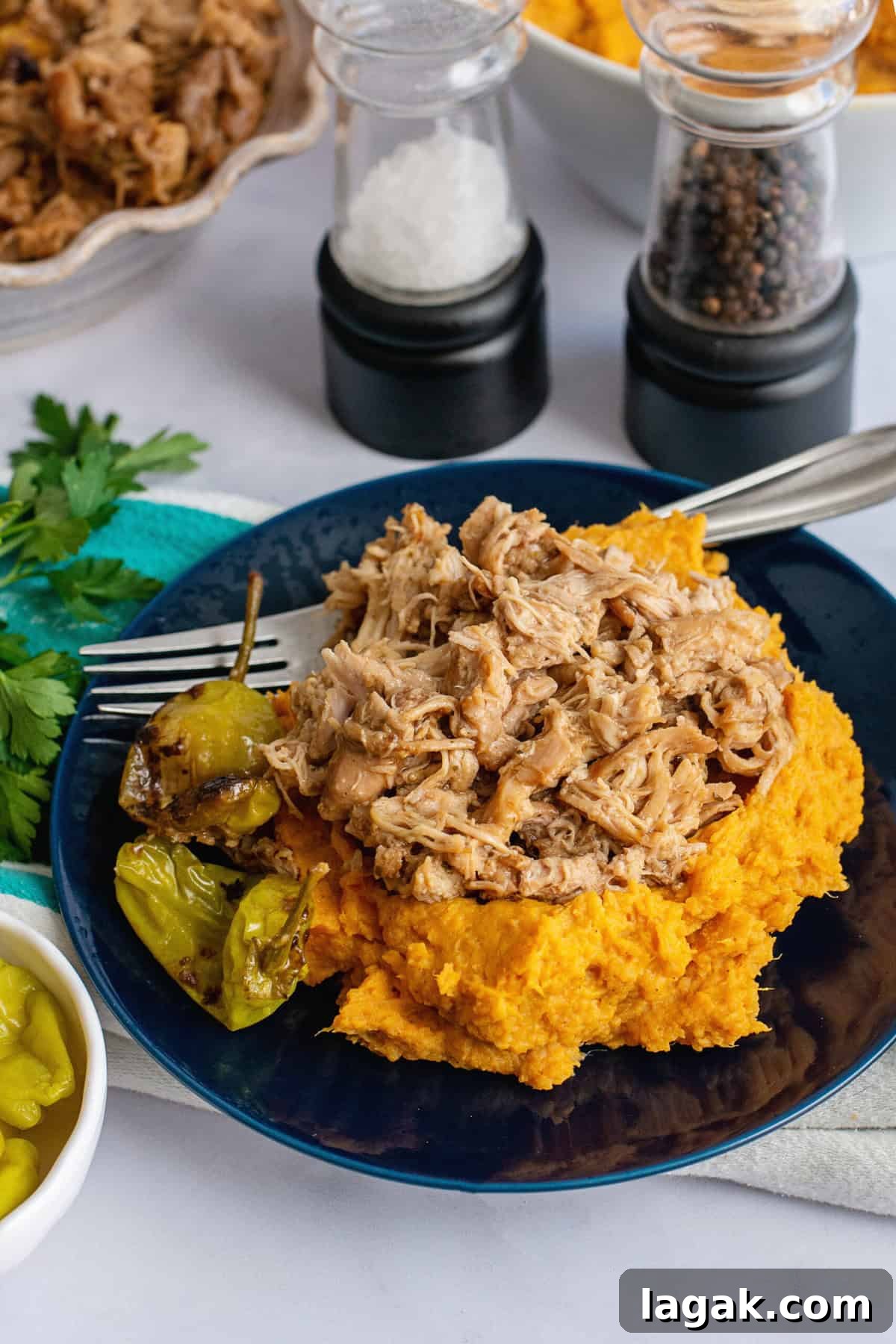Mississippi Chicken Served Over Creamy Mashed Sweet Potatoes 4 Plate of Mississippi chicken served over fluffy mashed sweet potatoes, garnished with pepperoncini peppers, with salt and pepper shakers, parsley, and a fork in the background for a comforting, savory meal presentation.