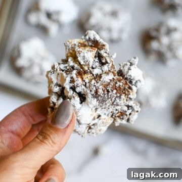 holding a muddy buddies cookie in front of a baking sheet full of cookies.
