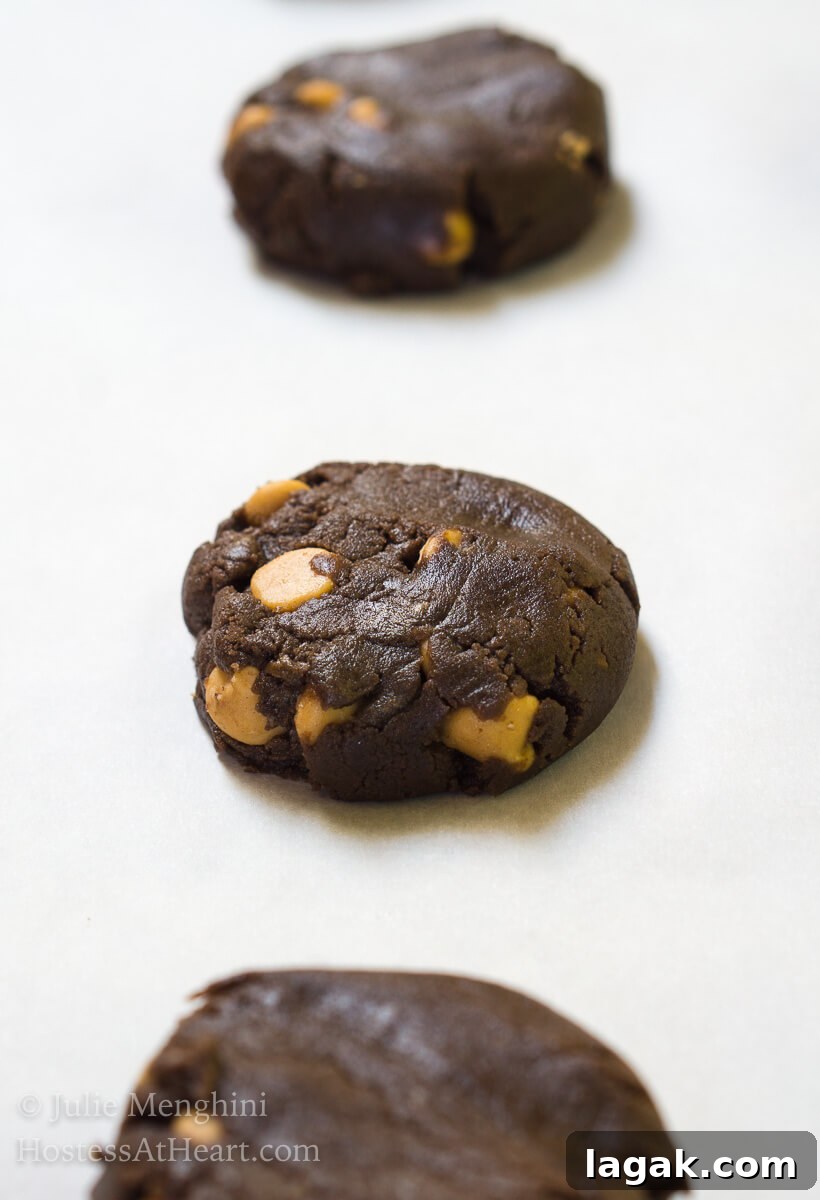 No-Chill Dark Chocolate Peanut Butter Cookie Recipe 6 Raw cookie dough of a chocolate cookie dotted with peanut butter chips sitting on white parchment paper.