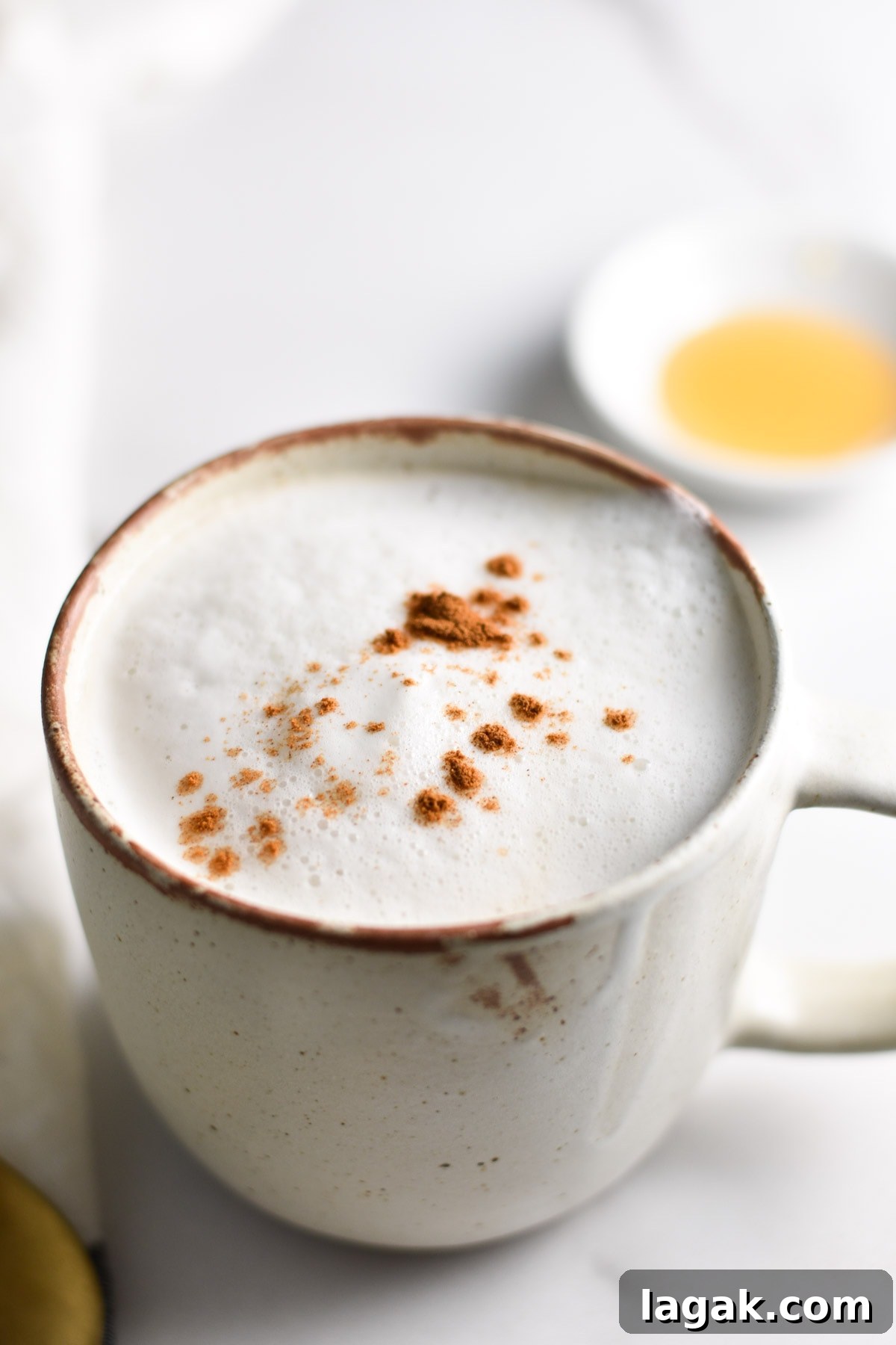 A frothed latte with tea next to a bowl of honey.