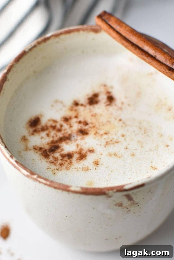 A mug of frothed cinnamon milk with a cinnamon stick and a napkin