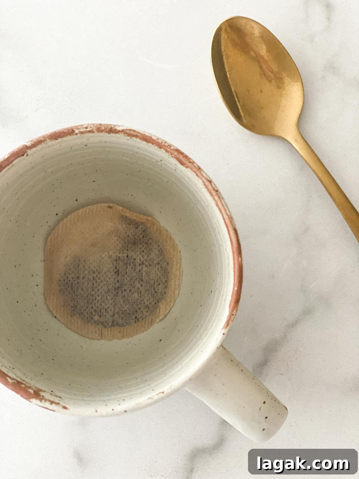 A tea bag in a mug next to a spoon.