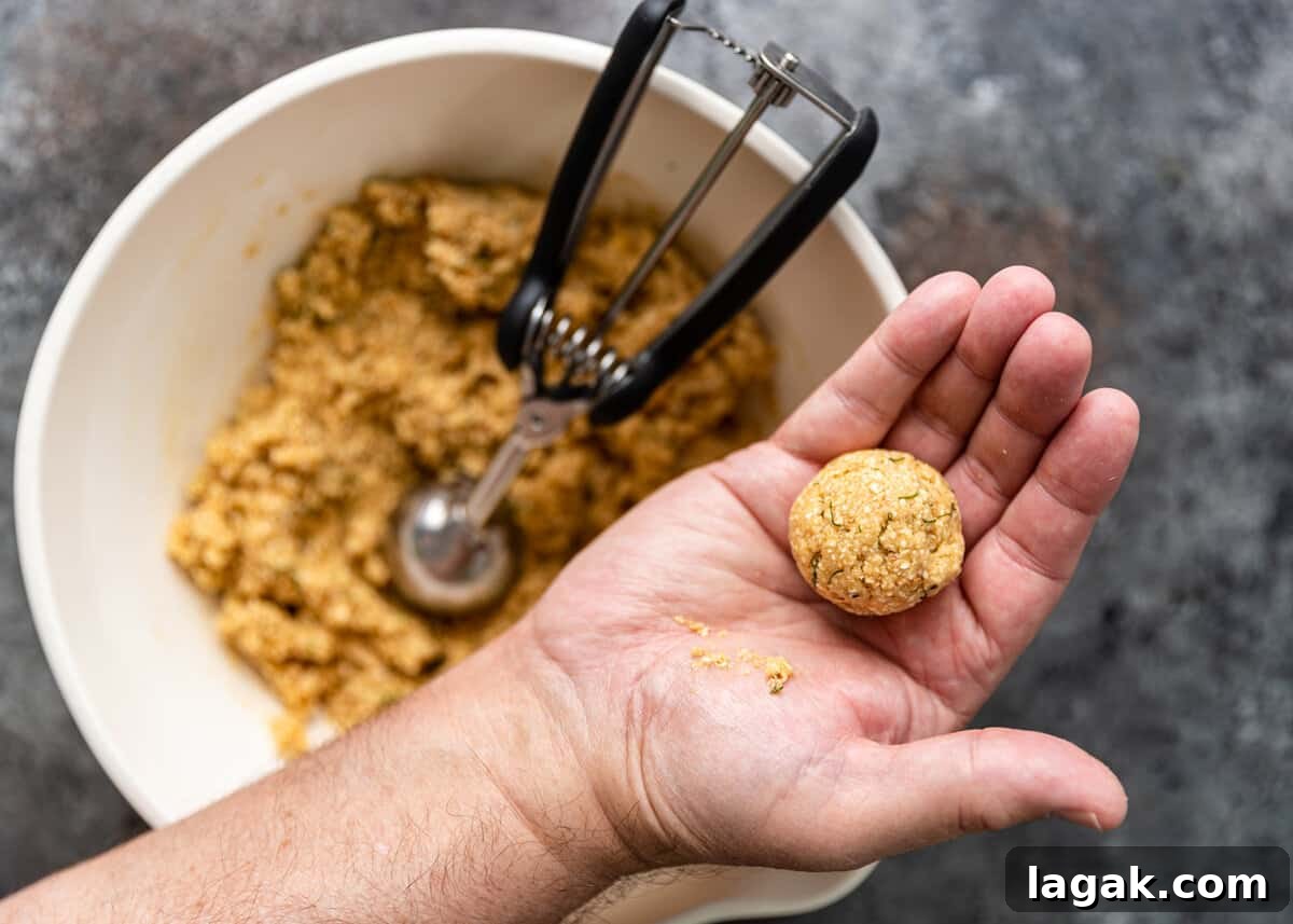 hand holding formed matzo ball overtop of mixing bowl with remaining ingredients with scooper