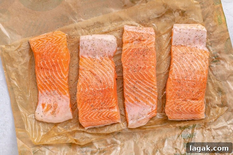 Salmon slices on parchment paper with salt and pepper.