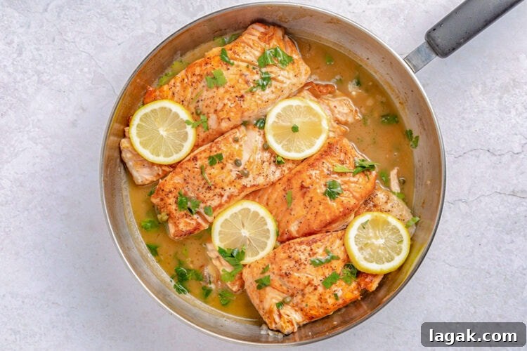 Salmon piccata in a large silver skillet with lemon coins and parsley to garnish.