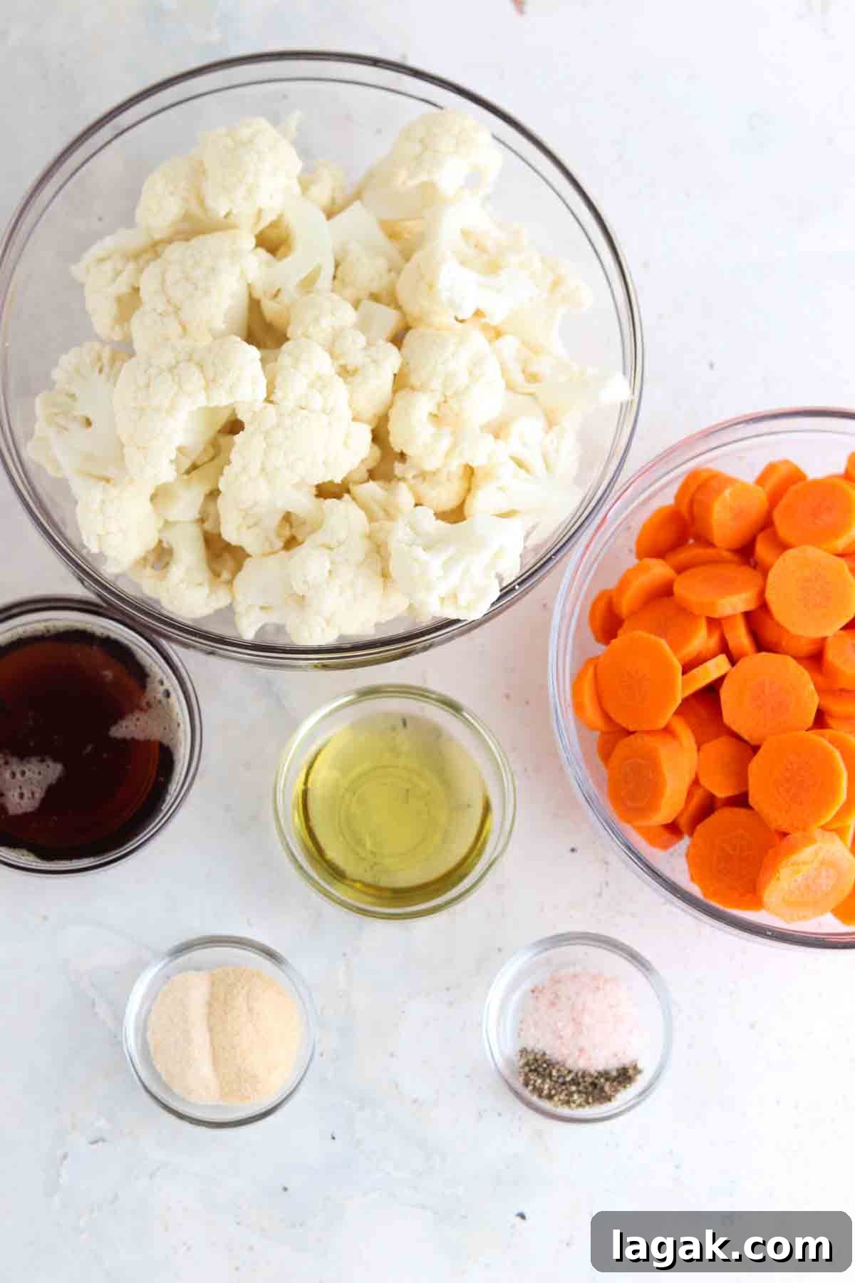 Carrots, cauliflower, seasoning, oil and maple syrup in small glass bowls on the counter. 
