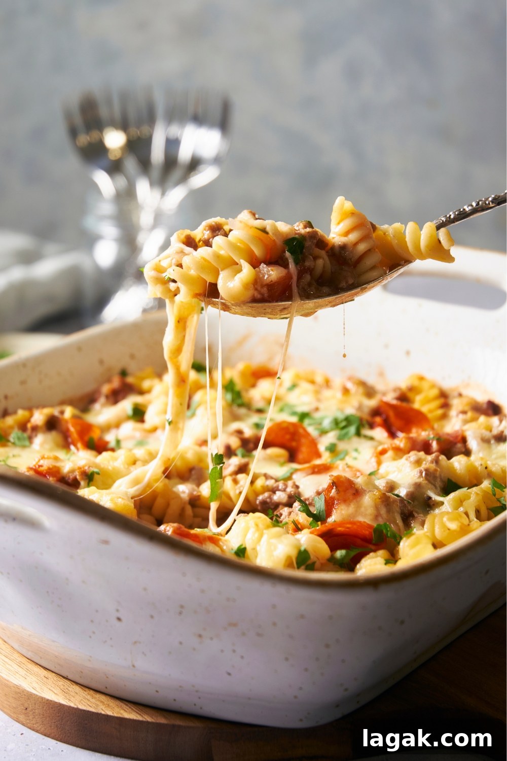 A deep baking dish with pizza pasta in it. A spoon has a scoop of the pasta pizza and is holding it over the dish.