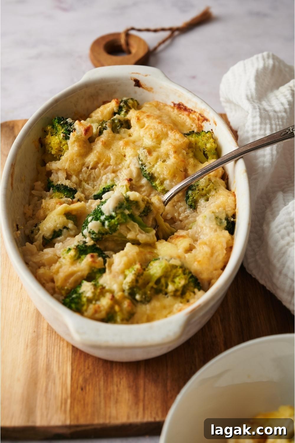 Broccoli rice casserole in a casserole dish on a wood board with a spoon in the dish.