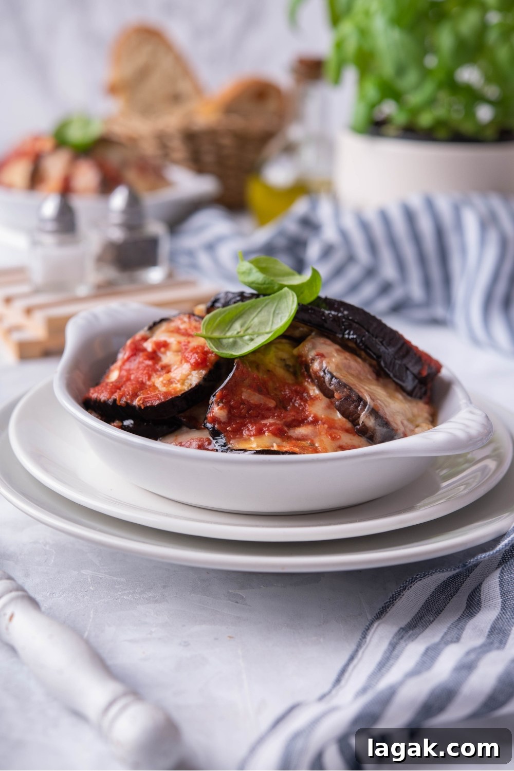 A white bowl filled with sliced eggplant with red sauce and melted cheese on top of them.