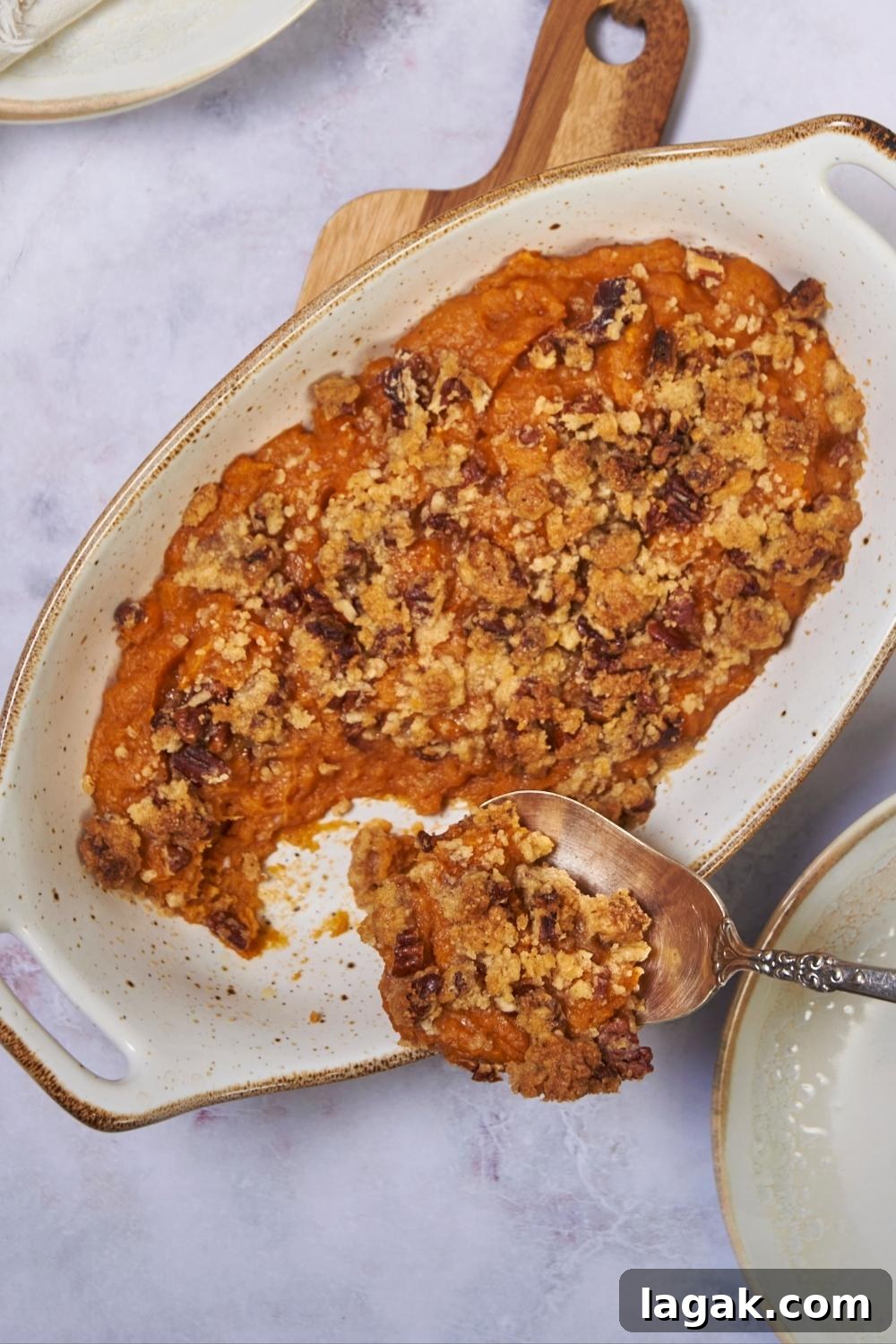 Ruth's Chris sweet potato casserole in a white baking dish with a serving being scooped out and put onto a plate.