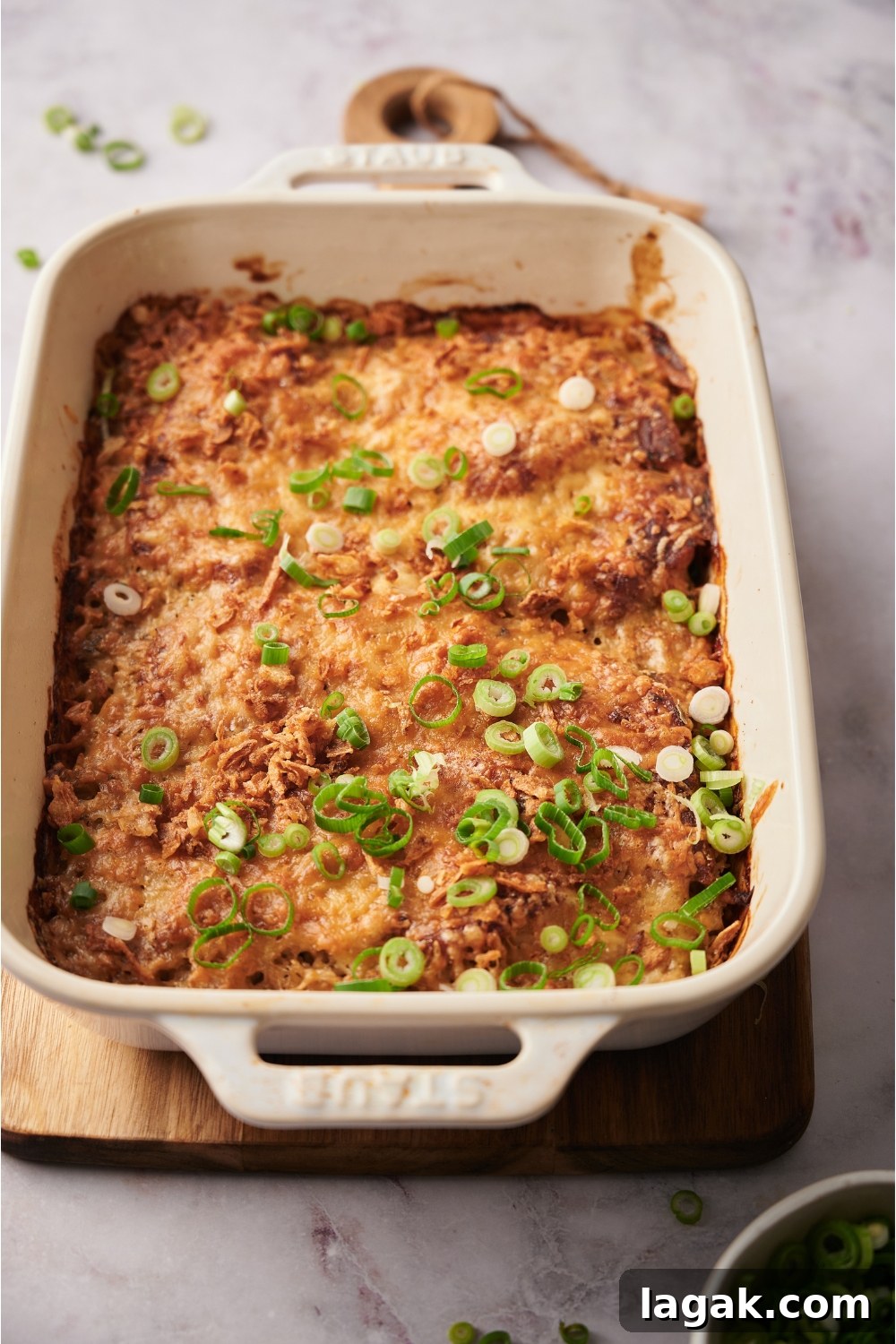 Green onions garnished on a freshly baked casserole in a white casserole dish that is on top of a wood board.