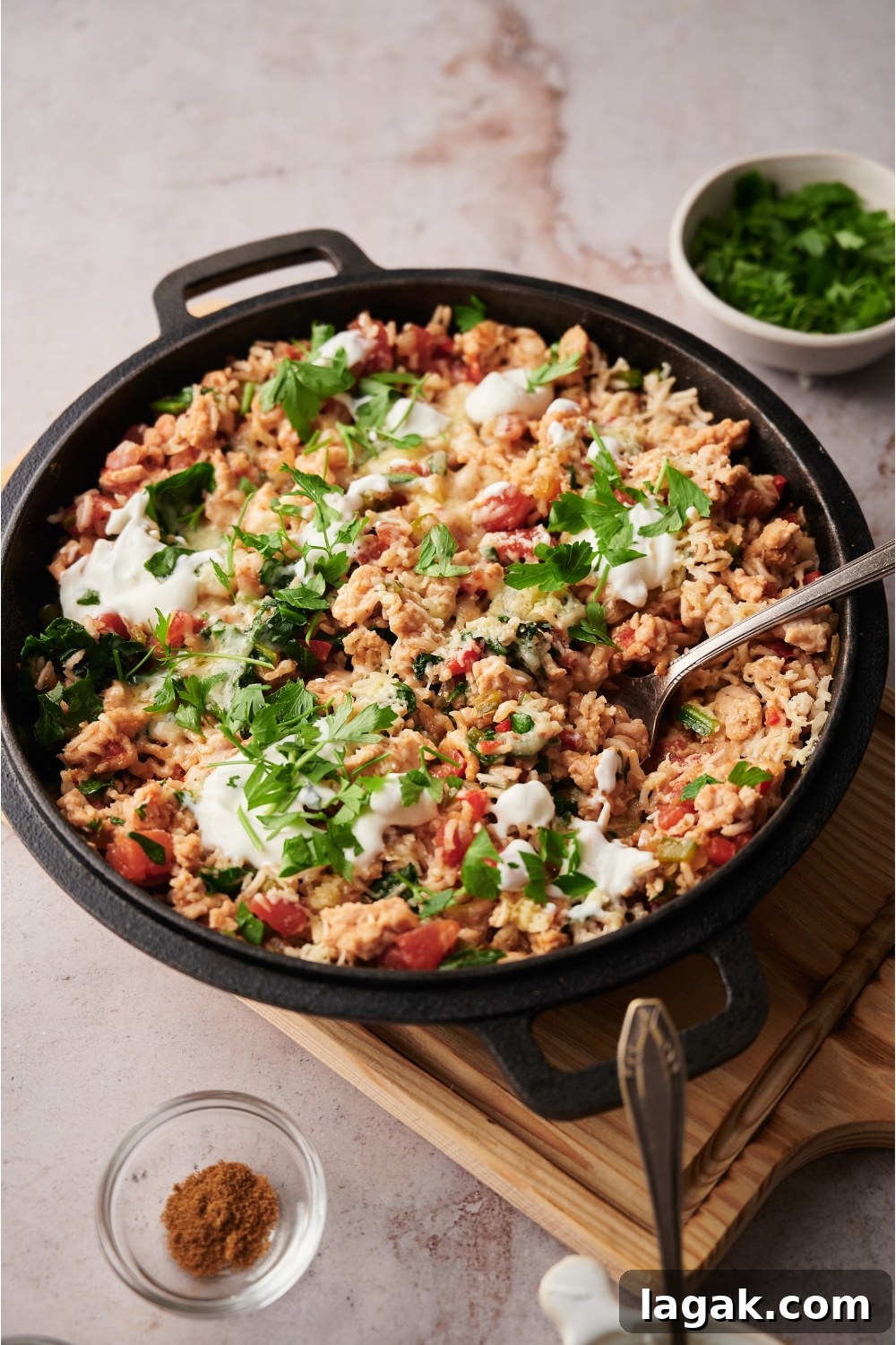 Black skillet on a wood board, filled with stuffed pepper casserole. There is a spoon in the pot and the casserole is topped with sour cream and fresh herbs.
