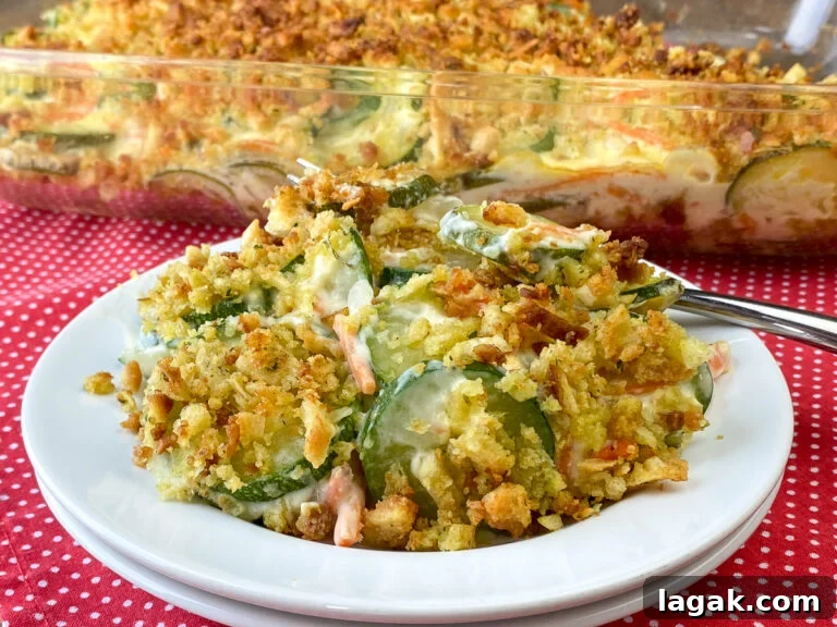 Close up pieces of lightly browned stuffing, shredded carrots and slices of zucchini on a white plate in front of full casserole dish