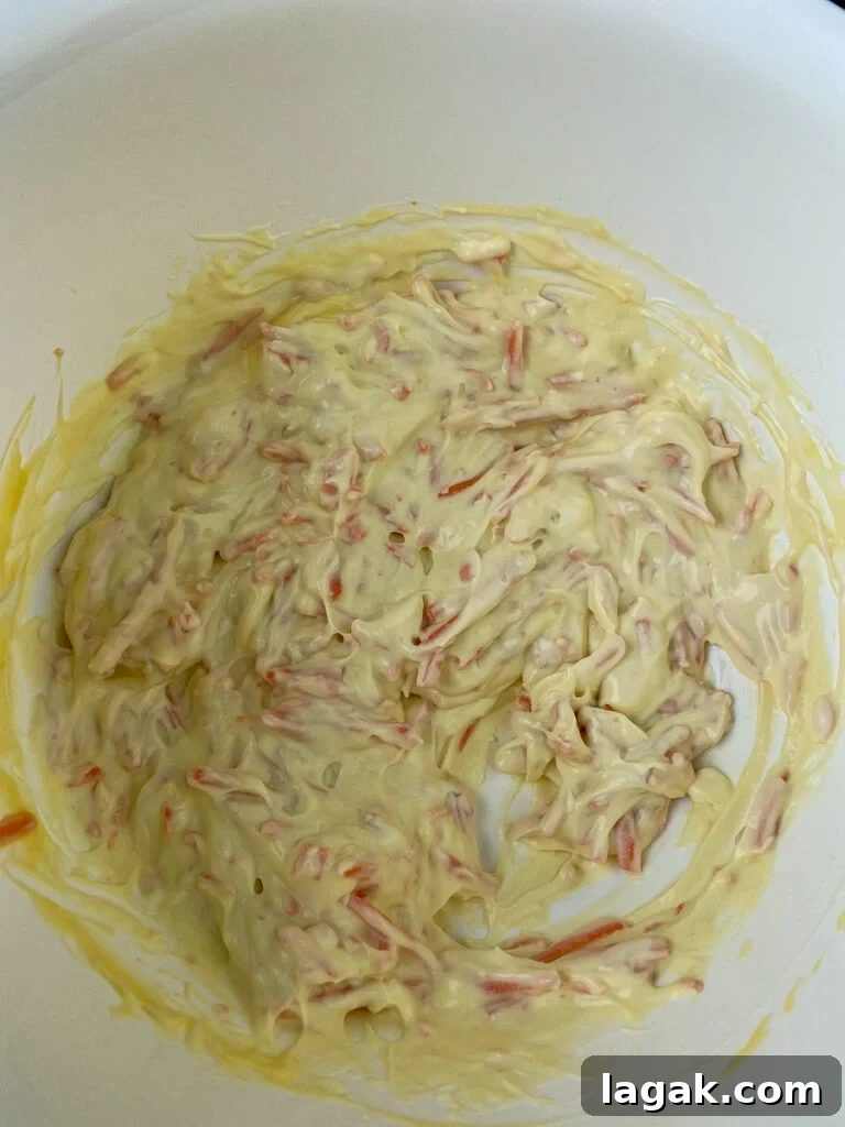 Shredded carrots, sour cream, condensed chicken soup in a white mixing bowl