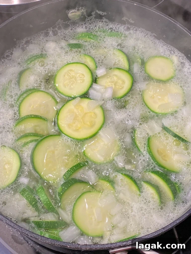 Sliced zucchini and chopped onions boiling in pot on the stove