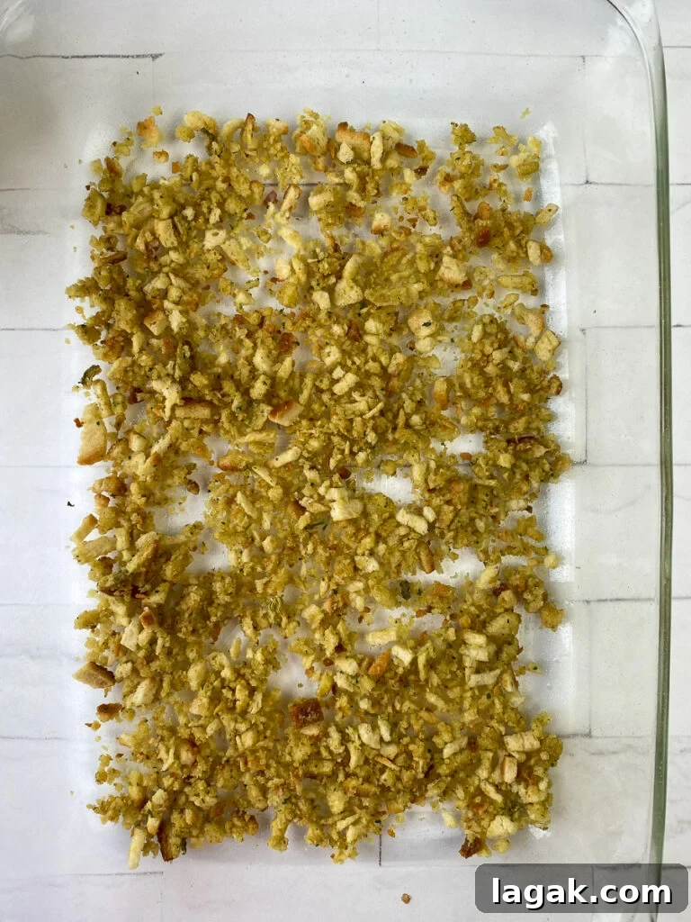 Half of stuffing mixture sprinkled in the bottom of a glass baking dish on a white counter top